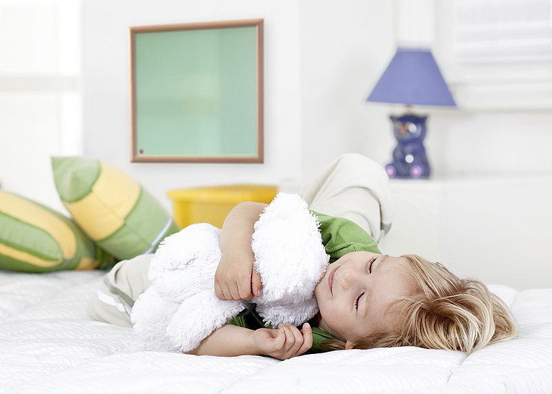 Infrarot - Heizpaneel an der Wand, davor ein schlafendes Kind im Bett